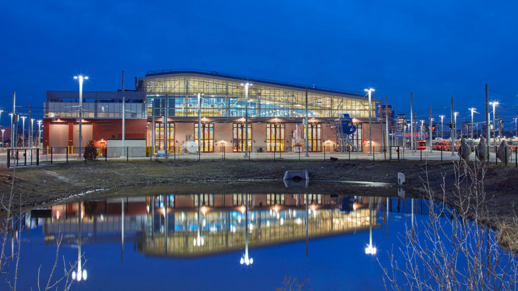 Exterior night photo of the facility in front of the storm water management pond