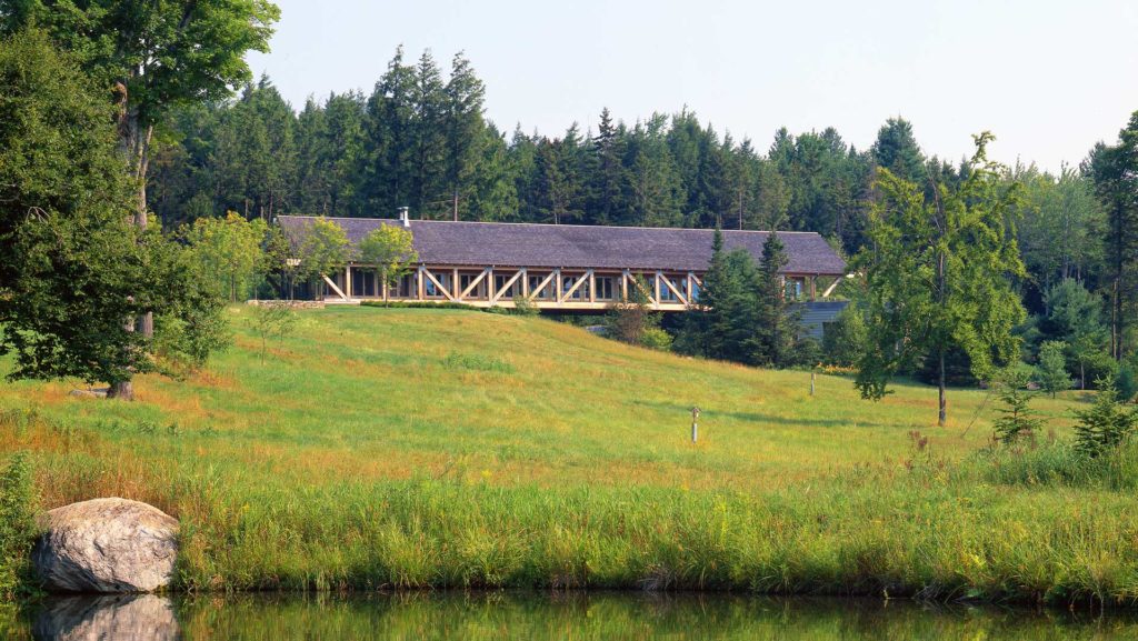 Exterior photo showing the entire bridge building, the pond and grassland in the front, and woods in the back
