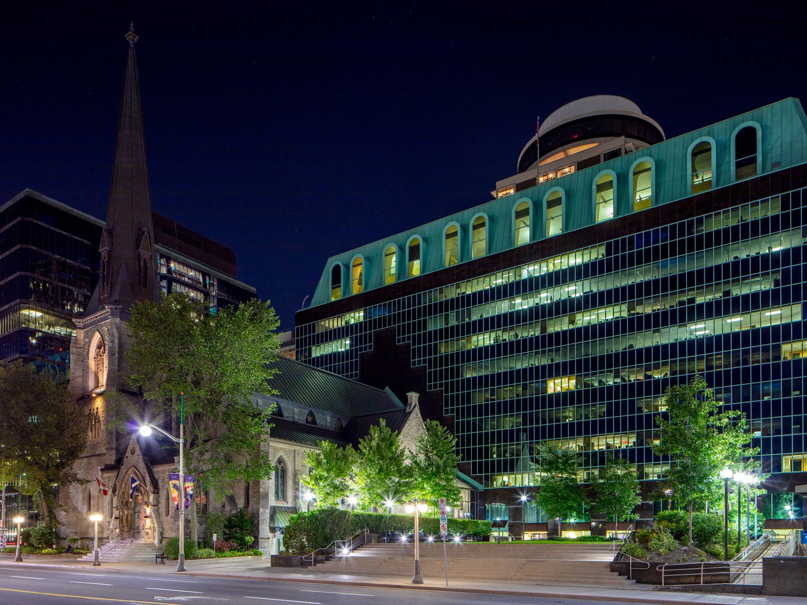 Exterior night photo of the building showing the church and landscape plaza