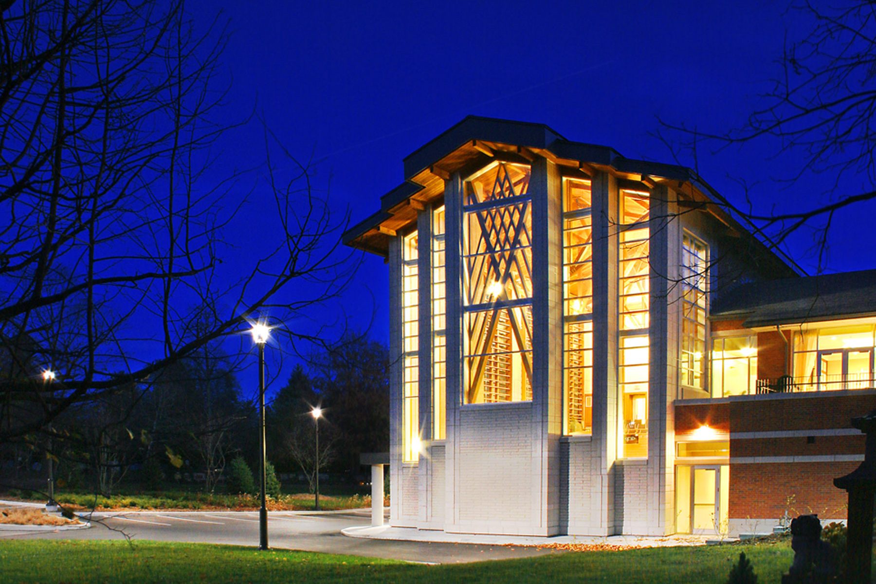 Exterior night photo of the chapel showing the glass wall, wooden roof and structures.